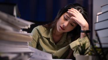 Persoon leunt op bureau met boeken, ziet er vermoeid uit.