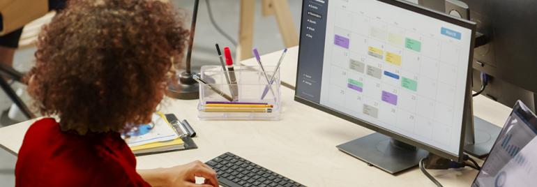 Vrouw met krullend haar zittend achter haar bureau kijkend naar haar computer